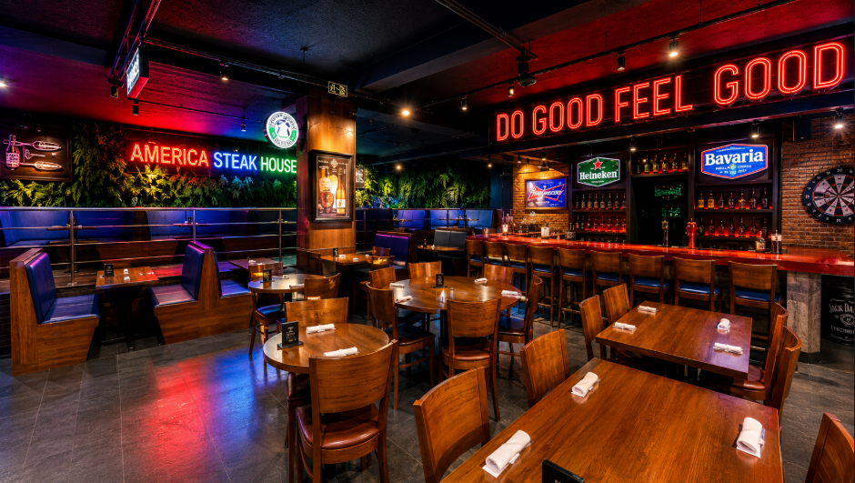 Salão interno de restaurante com mesas e bar ao fundo.